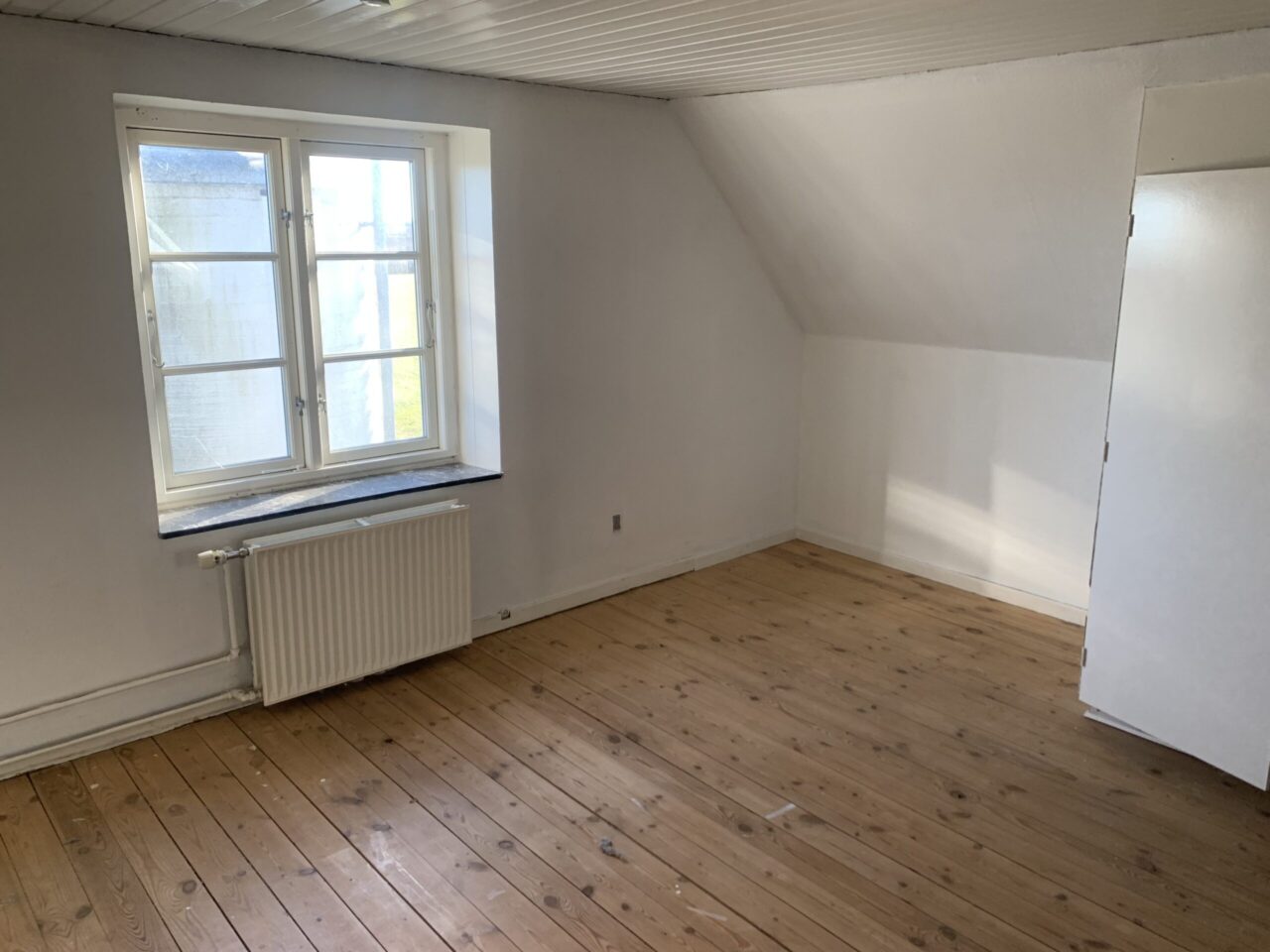 Investeringsejendom i Christiansfeld - Hvidt lokale med trægulv og et vindue