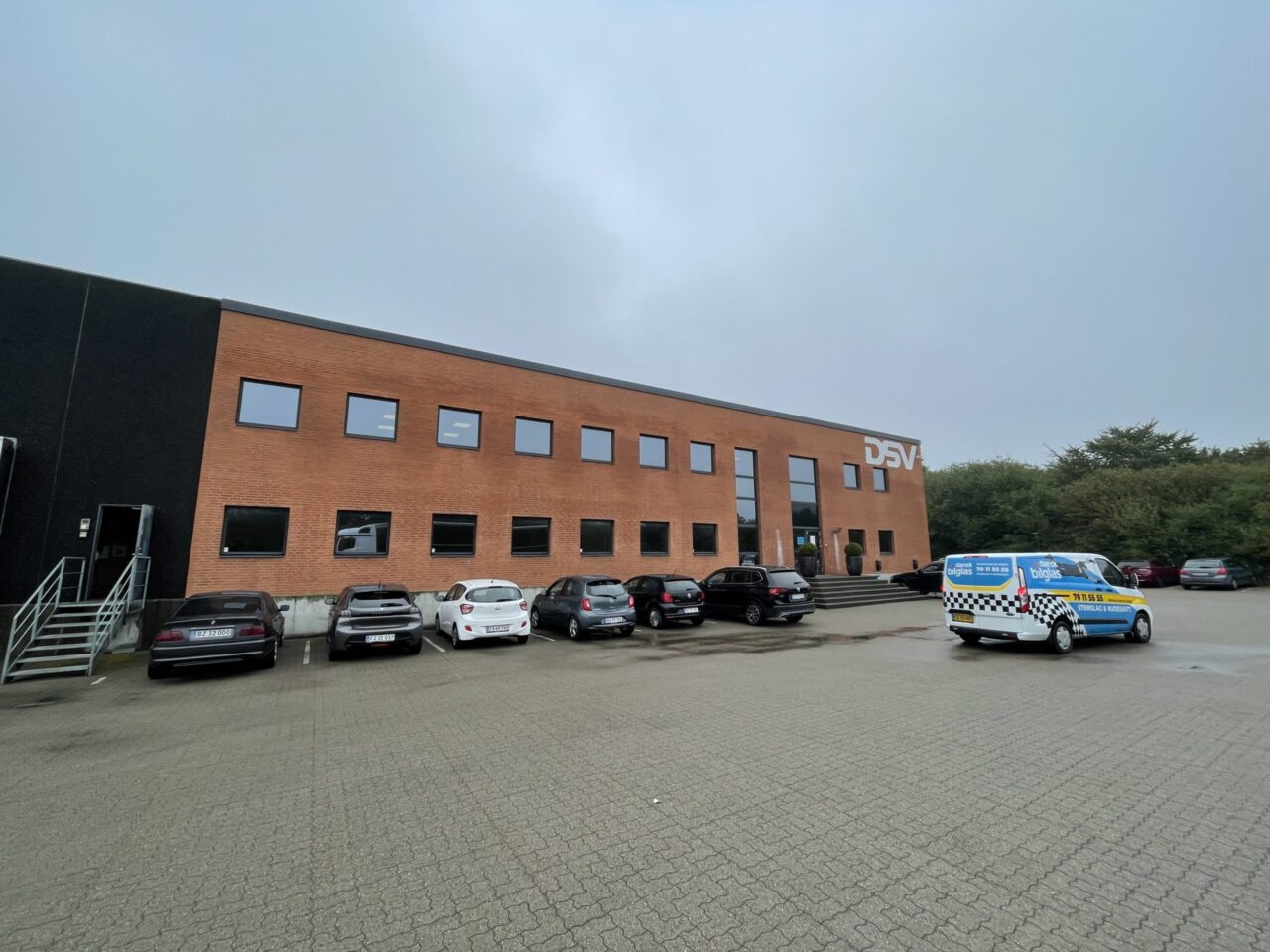 Kontor til leje i Kolding - Rød murstens bygning med stor parkeringsplads og mange biler