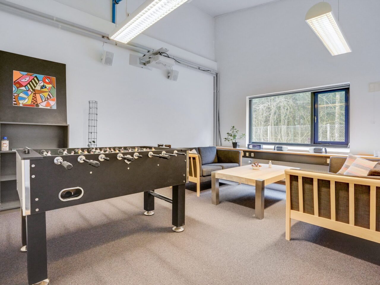 Kontorlokaler til leje i Vejen - Hvidt fælleslokale med lyst trægulv og et vindue, et bordfobold, sofa og kaffebord